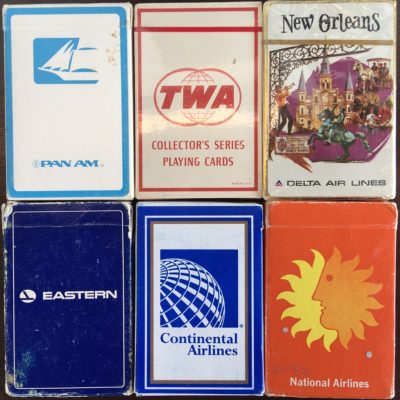 The image shows six vintage airline-themed playing card decks. The decks are arranged in two rows of three. From left to right, the top row features:

1. A Pan Am deck with a blue and white design.
2. A TWA (Trans World Airlines) deck labeled "Collector's Series Playing Cards" with a red and white design.
3. A Delta Air Lines deck with a New Orleans theme, featuring an illustration of a historic building and a horse statue.

The bottom row features:

1. An Eastern Airlines deck with a dark blue design.
2. A Continental Airlines deck with a blue and white globe design.
3. A National Airlines deck with an orange design featuring a sun with a face.