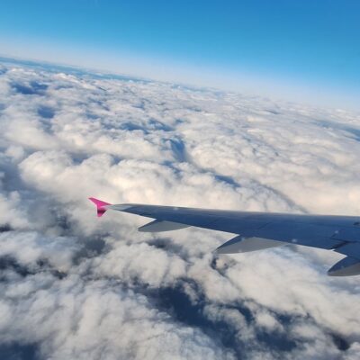 pink wingtip against a partly cloudy sky and horizon while flying