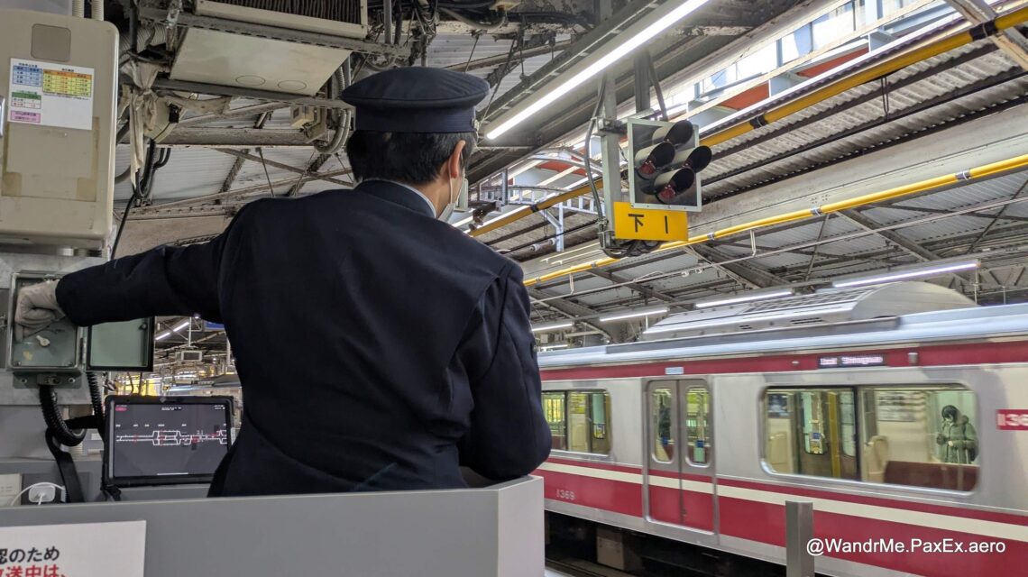 Back of a man coordinating trains in Japan from a podium on a platform