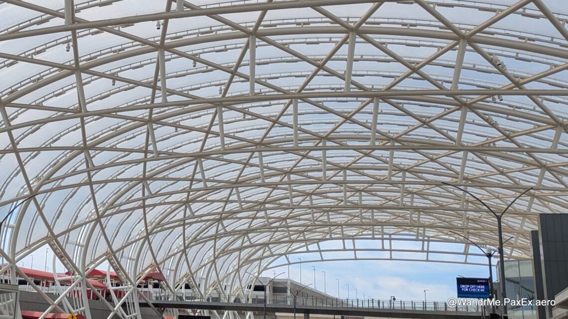 arched metal structure holding up a glass awning over an airport roadway drop off area.