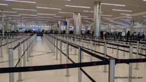 Large security area at an airport, mostly empty, with lots of black tensabarrier lanes.