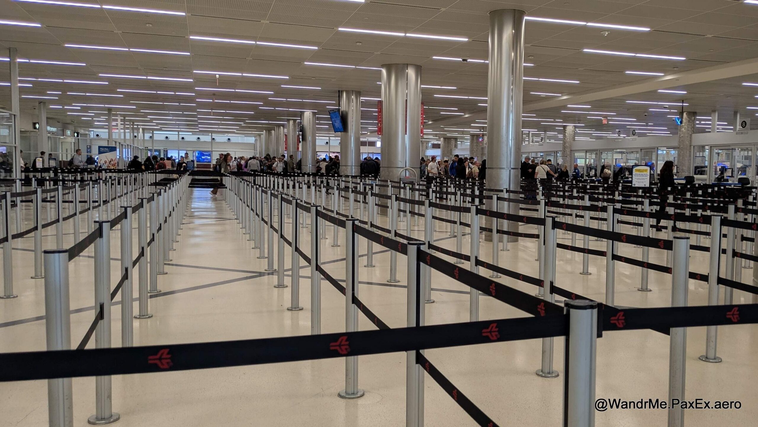 Large security area at an airport, mostly empty, with lots of black tensabarrier lanes.