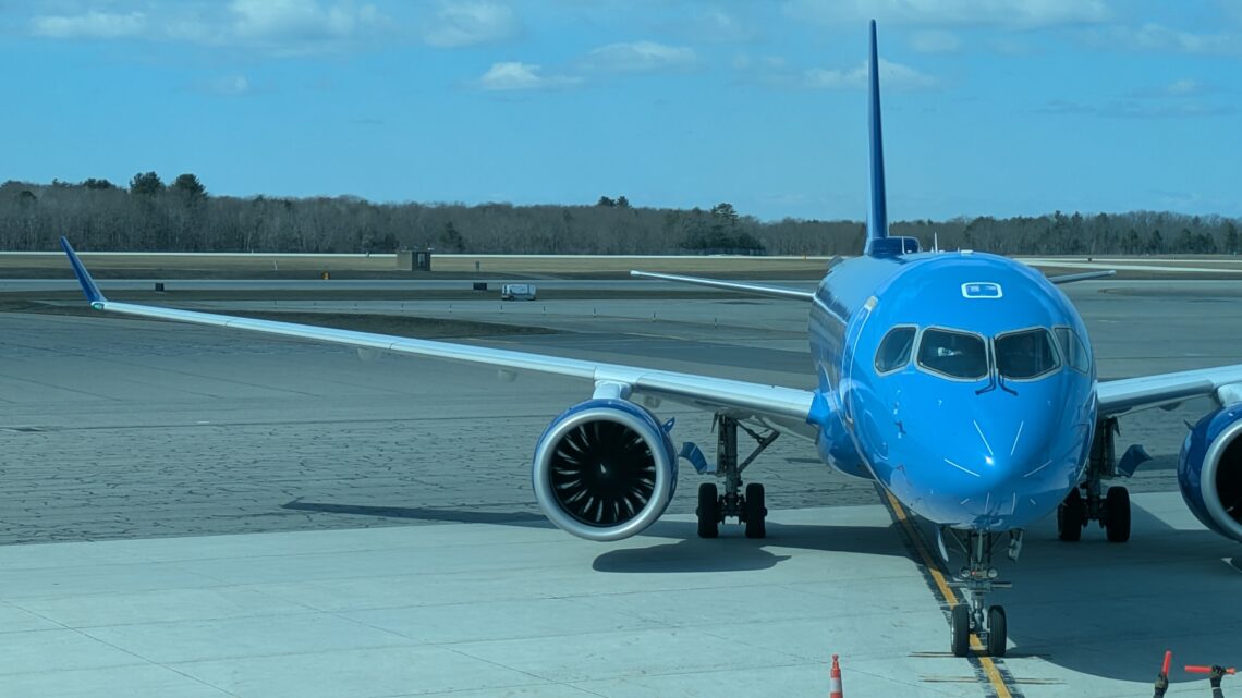Blue A220 from Breeze parked at a gate