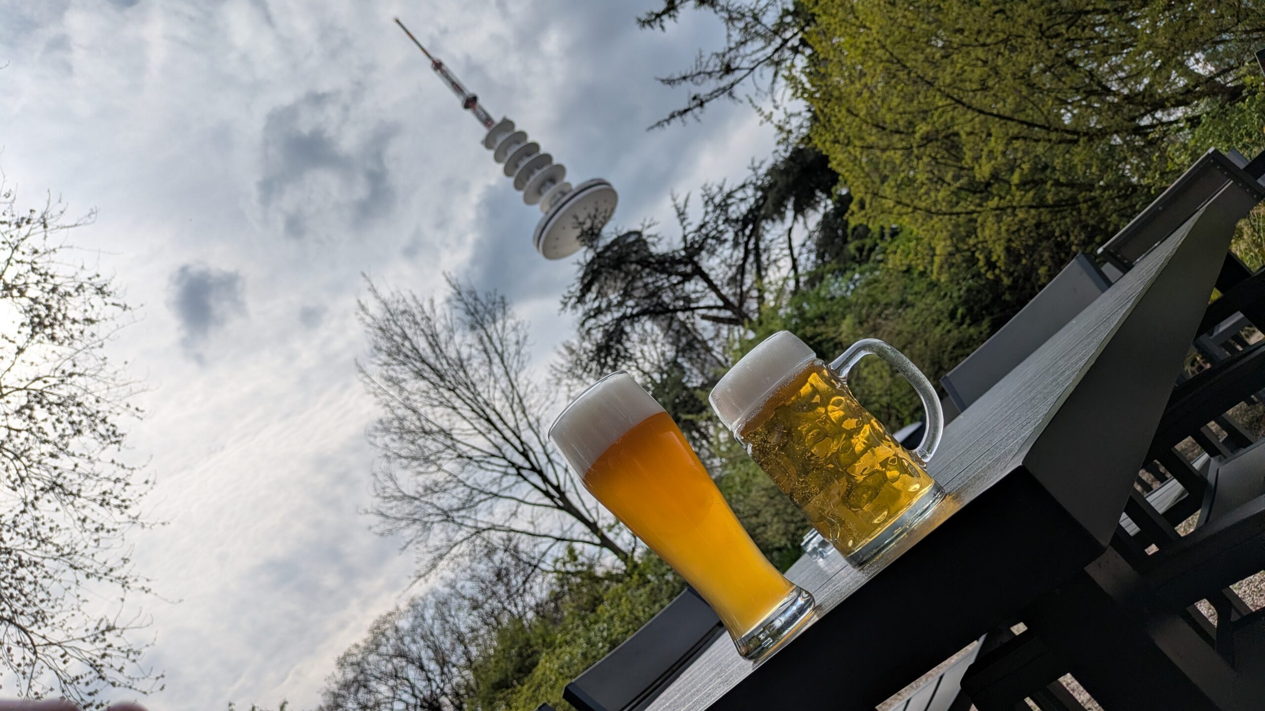 two beers on a table in a biergarten with a giant round radio tower behind